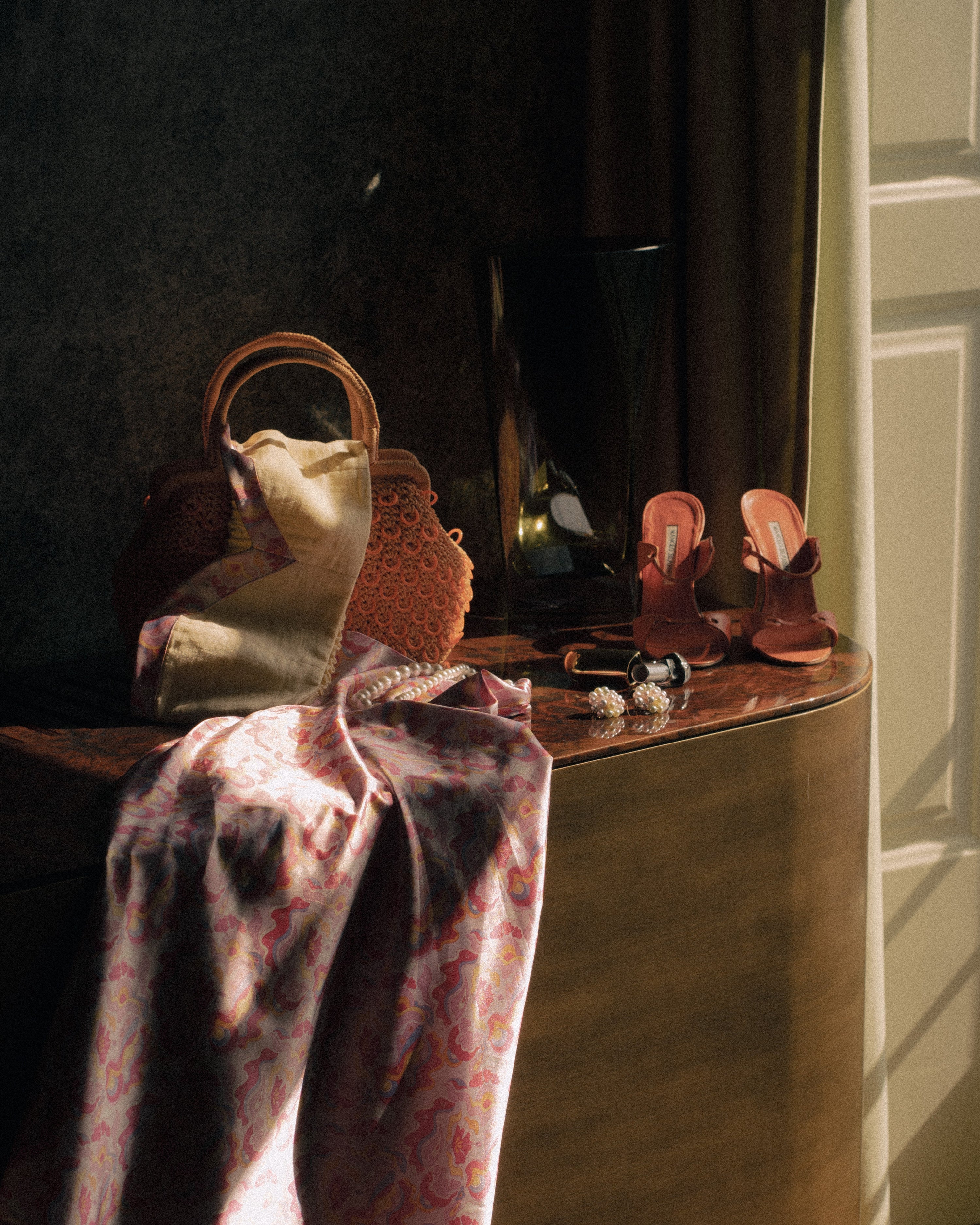 <img src="prompscampaign" alt="The Guava Glow Skirt and Sunny Chic Top styled on a hotel room console, paired with aesthetic accessories like vintage Manolo Blahnik shoes and a 70s orange raffia bag. A breezy resortwear look for sunny getaways.">