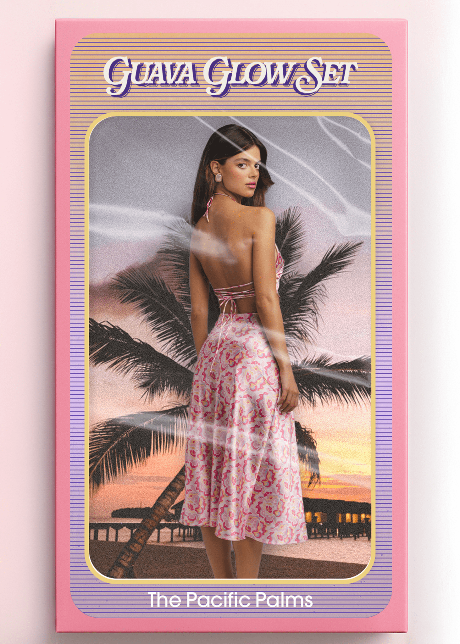 <img src="guavaglowback" alt="Guava Glow Set – The Pacific Palms. Model shown from the back inside a vintage doll-style packaging box, wearing a pink satin retro pattern co-ord outfit with white trim. Styled like a retro toy against a sunset beach with palm trees and overwater bungalows.">