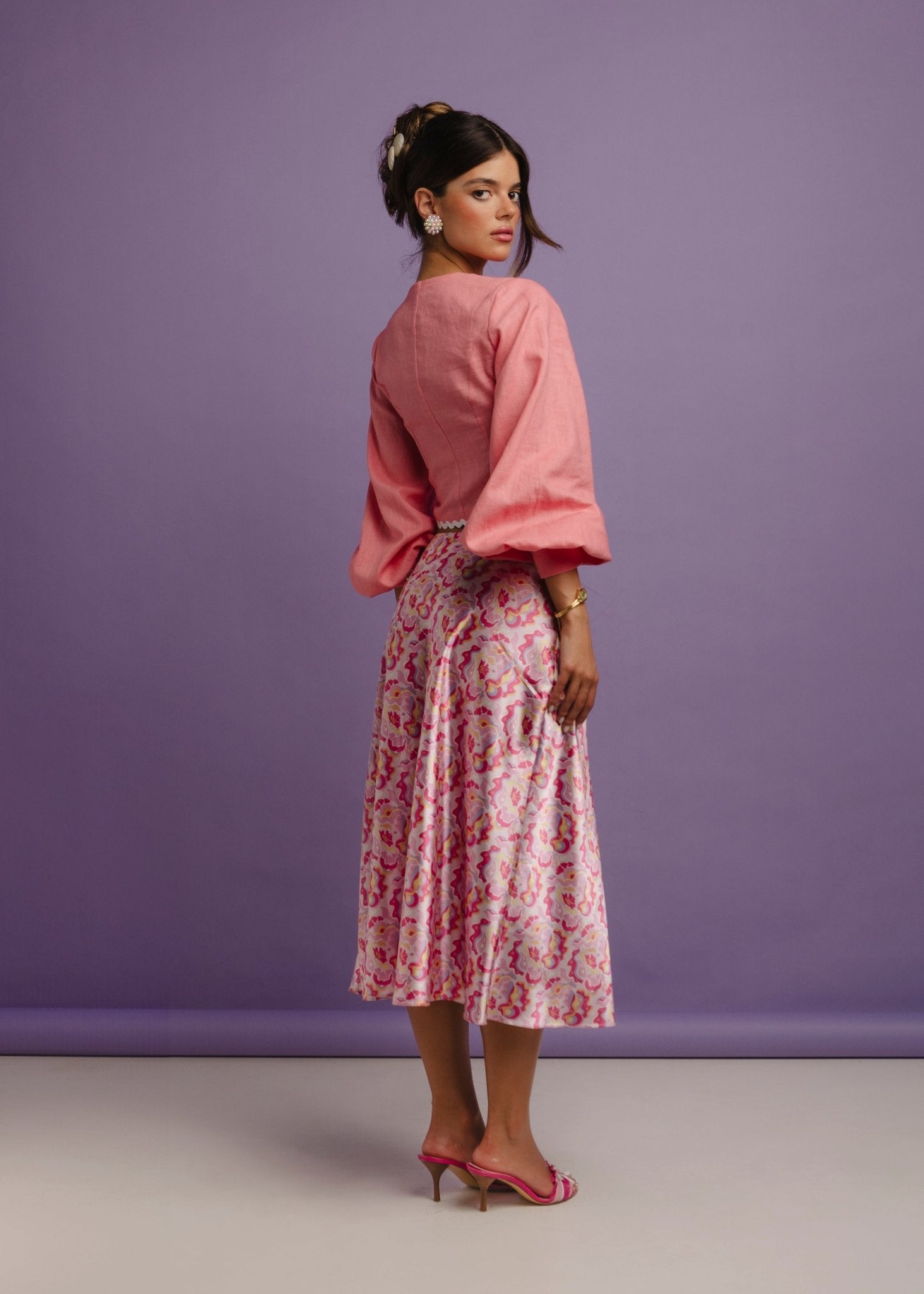 <img src="guavaglowskirtfulllookcloseup" alt="Back view of a Model wearing a pink retro pattern satin skirt with a flattering bias cut. and a pink linen top. Perfect outfit for a brunch at the beach club.">