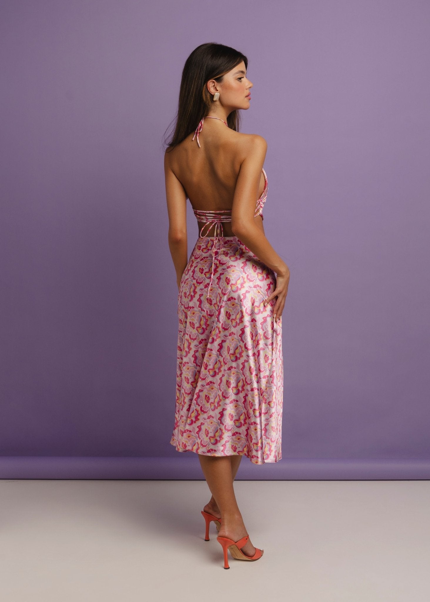 <img src="guavaglowskirtfulllookbackview" alt="Full back view of a Model wearing a pink retro pattern satin skirt with a matching top with back ties.">