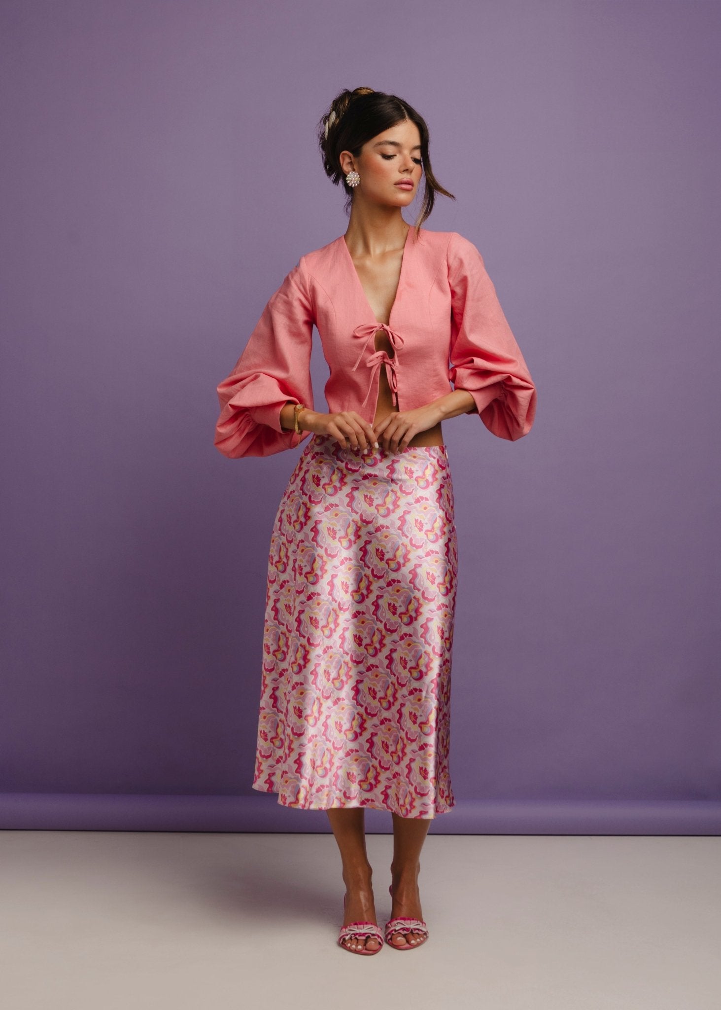 <img src="guavaglowskirtfulllookfront" alt="Front view of a Model wearing a pink retro pattern satin skirt with a flattering bias cut and a pink linen top. Perfect outfit for a brunch at the beach club.">