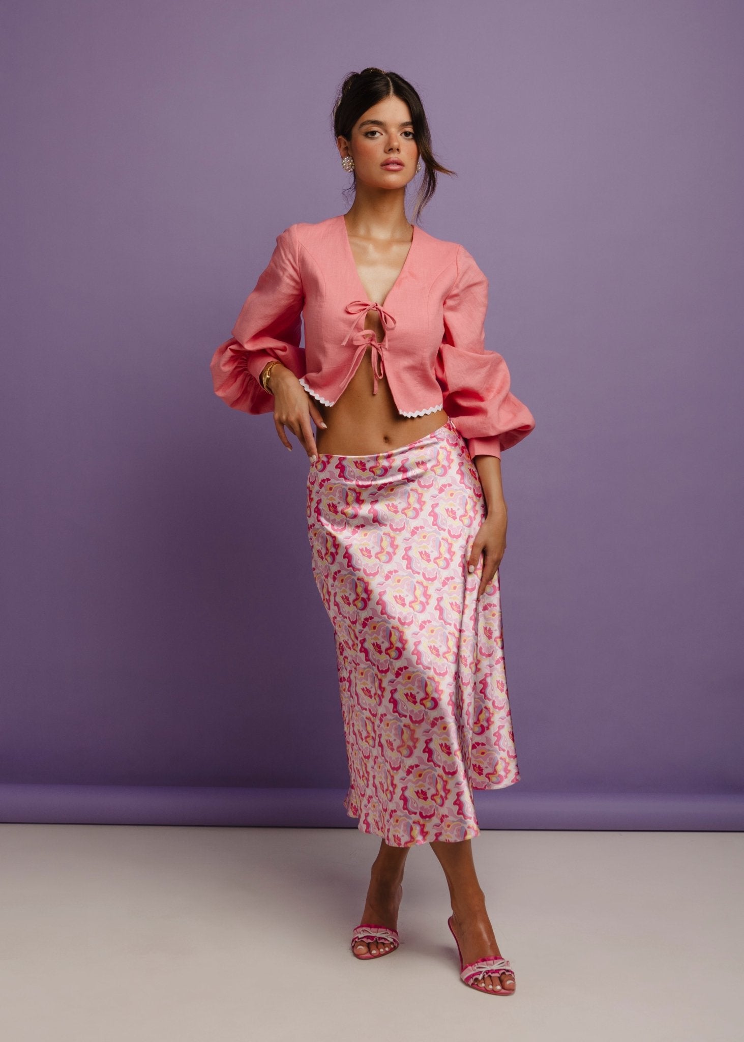<img src="guavaglowskirtfulllookfront2" alt="Front view of a Model wearing a pink retro pattern satin skirt with a flattering bias cut and a pink linen top. Perfect outfit for a brunch at the beach club.">