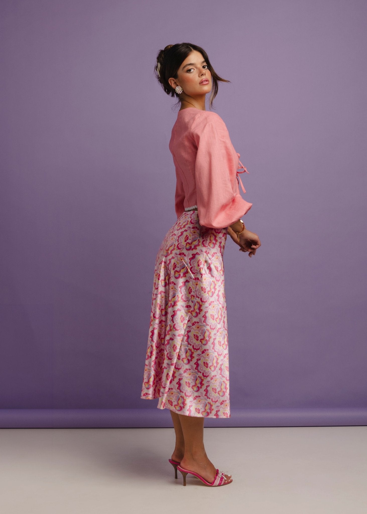 <img src="guavaglowskirtfulllooklateral" alt="Lateral view of a Model wearing a pink retro pattern satin skirt with a flattering bias cut. and a pink linen top. Perfect outfit for a brunch at the beach club.">