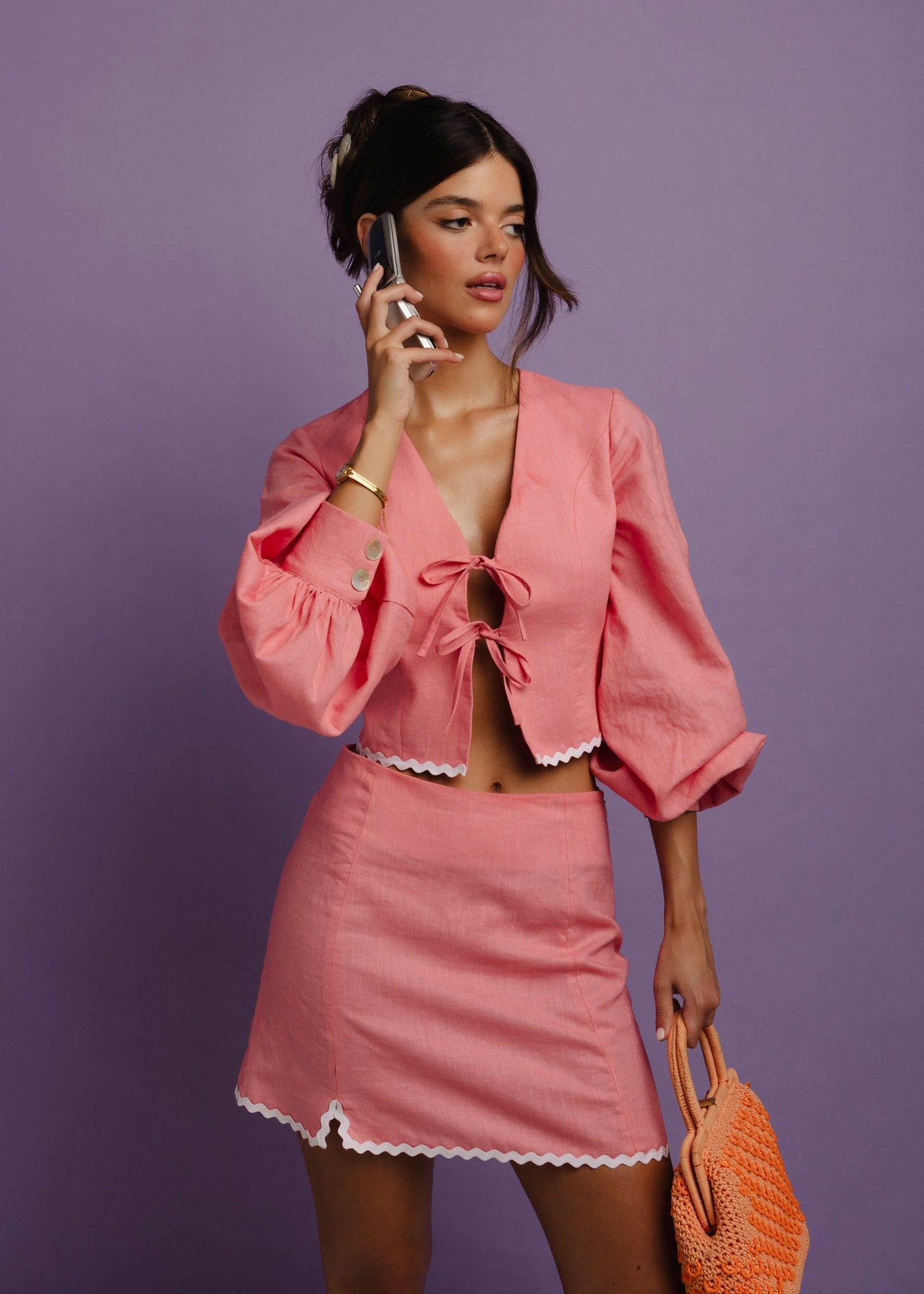 <img src="islandcrushtopmidbody" alt="Model wearing a pink linen medium top with two bows, 3/4 balloon sleeves, a white trim and a matching skirt, holding an orange oven bag and a 90s phone.">  