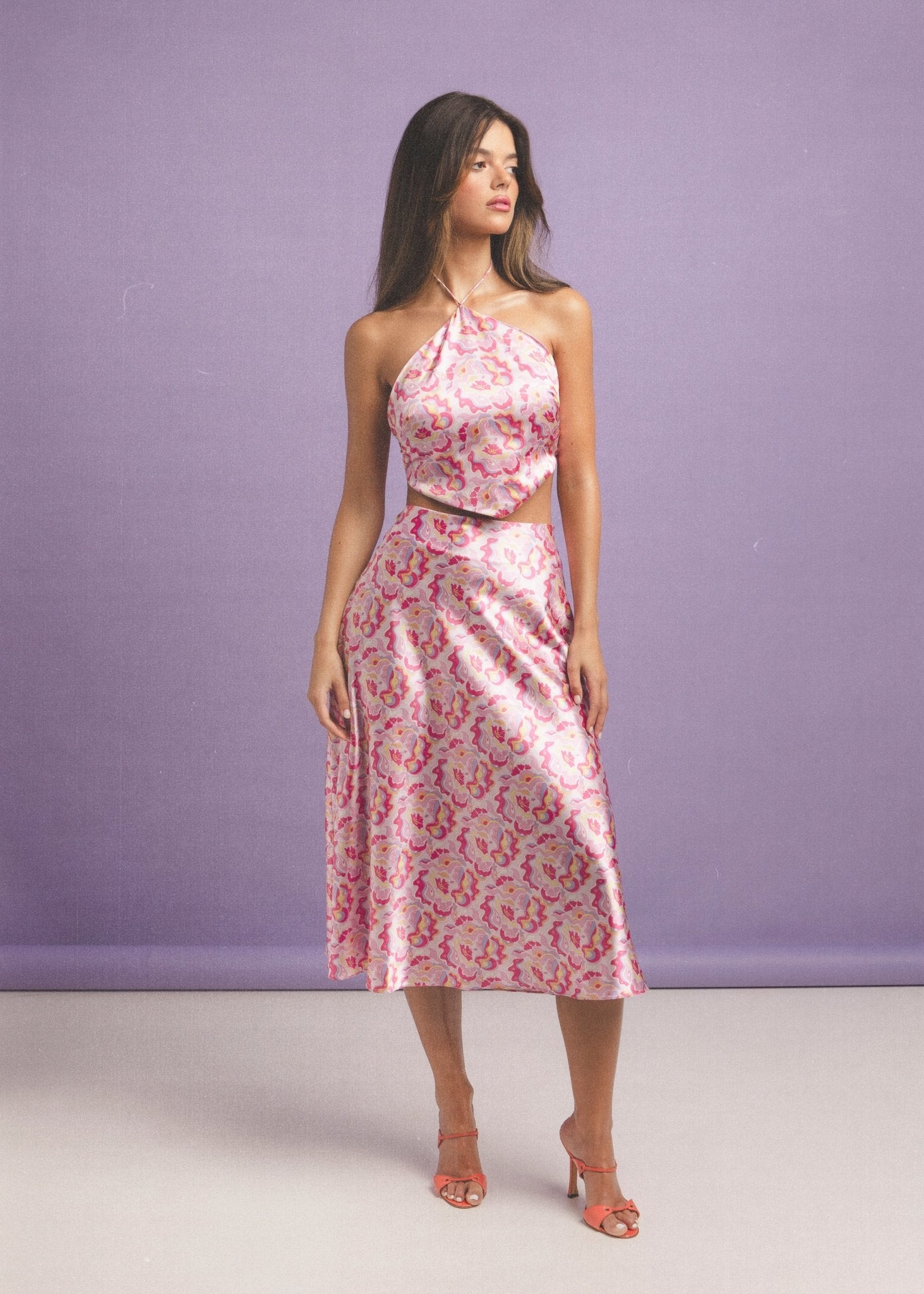 <img src="guavaglowtopfulllook" alt="Full view of a Model wearing a pink retro pattern satin top with V shape style hem, styled with a matching midi skirt and orange vintage sandals.">